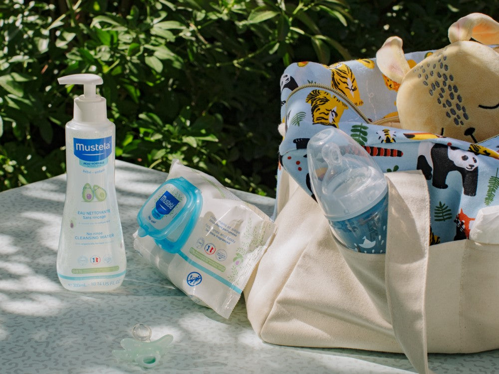 Mustela No-Rinse Cleansing Water, pump bottle beside a changing bag and a baby bottle