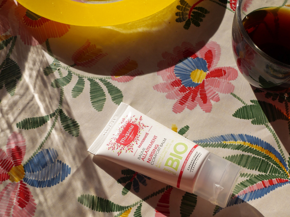 Mustela Organic Nursing Balm, tube on an embroidered floral tablecloth