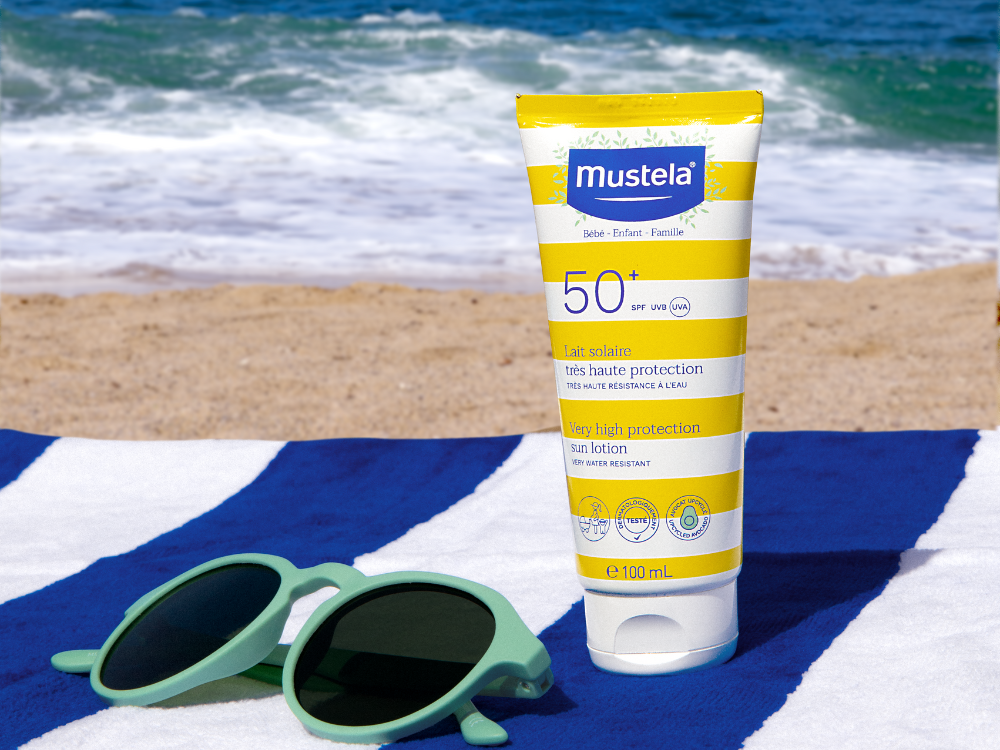 Mustela Lait Solaire, tube and sunglasses on a striped beach towel