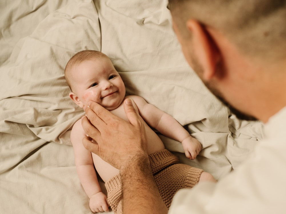 Mustela Stelatopia+, father's hand on a smiling baby's cheek
