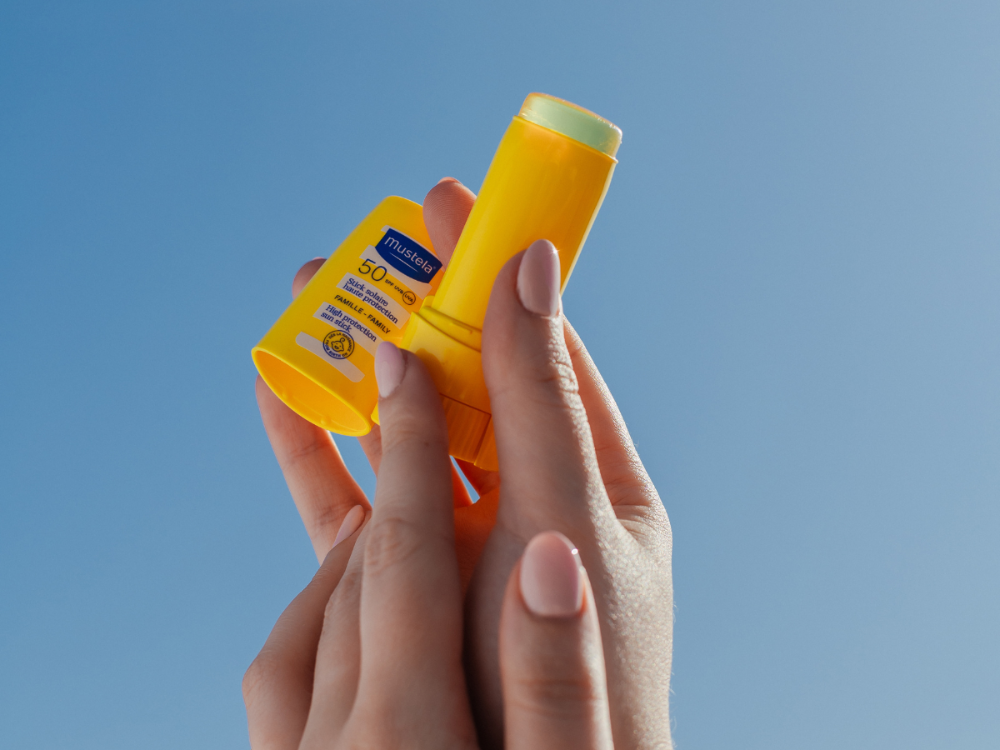 Mustela Sun Stick, hands holding the uncapped stick against a blue sky