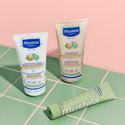 Mustela Universal Balm, tube lying beside two hair care tubes on green tiles