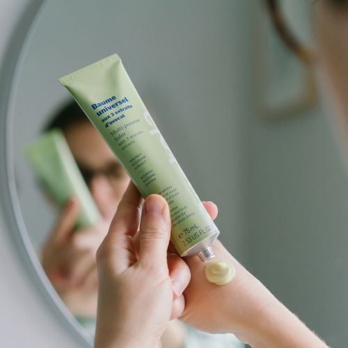 Mustela Universal Balm, woman squeezing balm onto her hand by a mirror