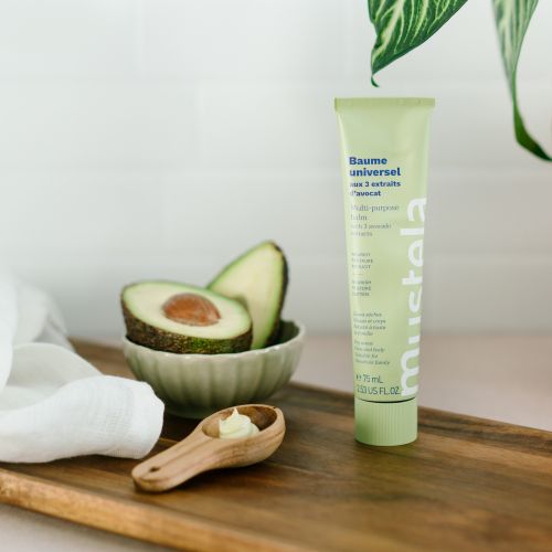 Mustela Universal Balm, tube beside avocado halves and a spoon of balm