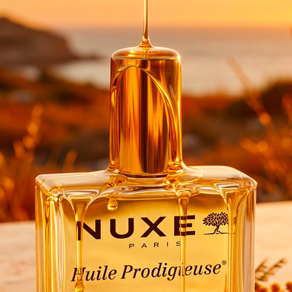 NUXE Huile Prodigieuse, bottle with dripping oil against a seaside sunset