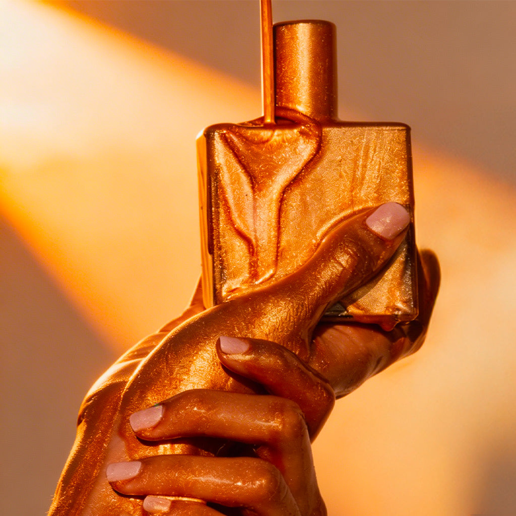 NUXE Huile Prodigieuse Gold, gold-coated hands holding the bottle in warm light
