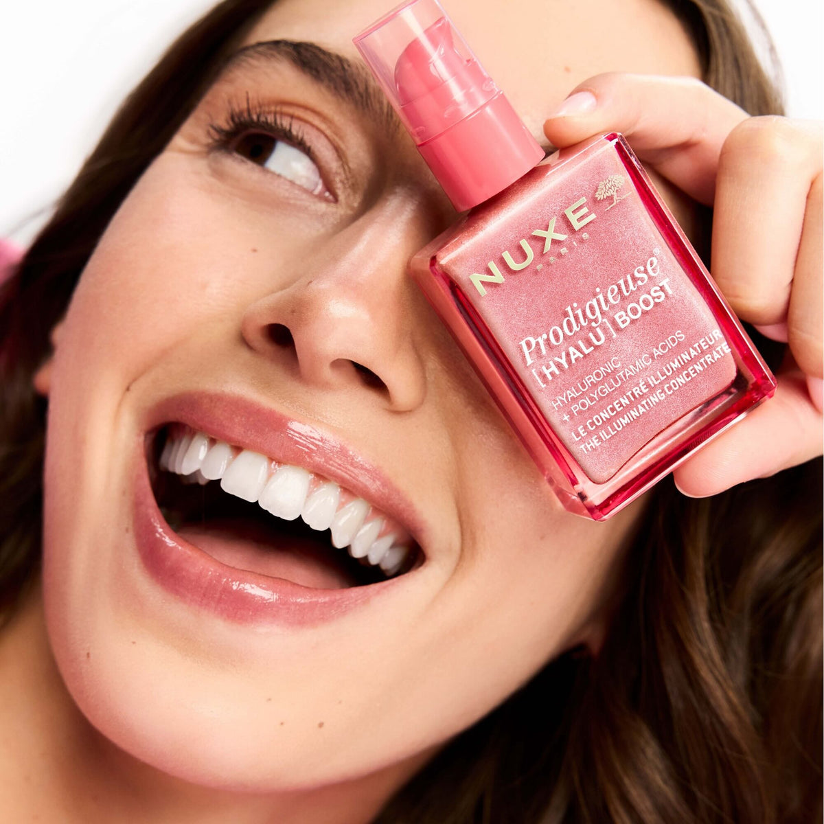 NUXE Prodigieuse Hyalu Boost, laughing woman holding the pump bottle over one eye
