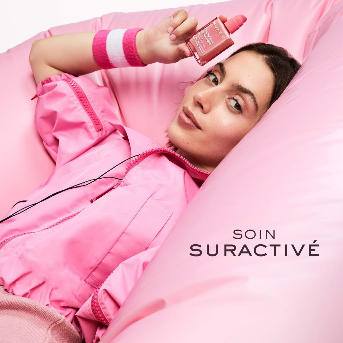 NUXE Prodigieuse Hyalu Boost, woman lounging on pink cushions holding the bottle, text in French