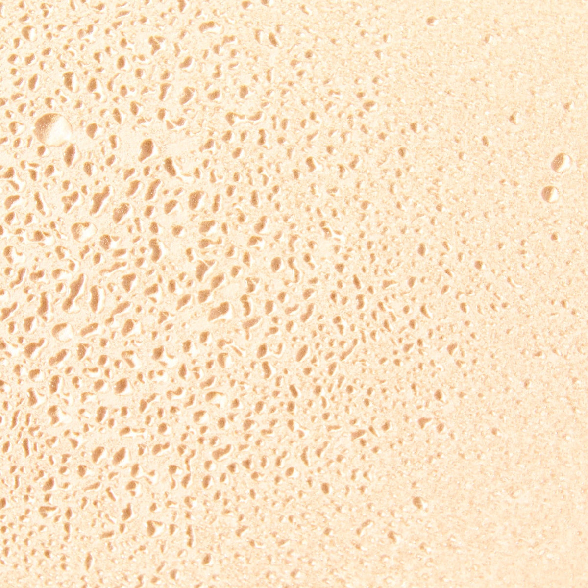 NUXE Prodigieux, close-up of golden droplets on a beige surface