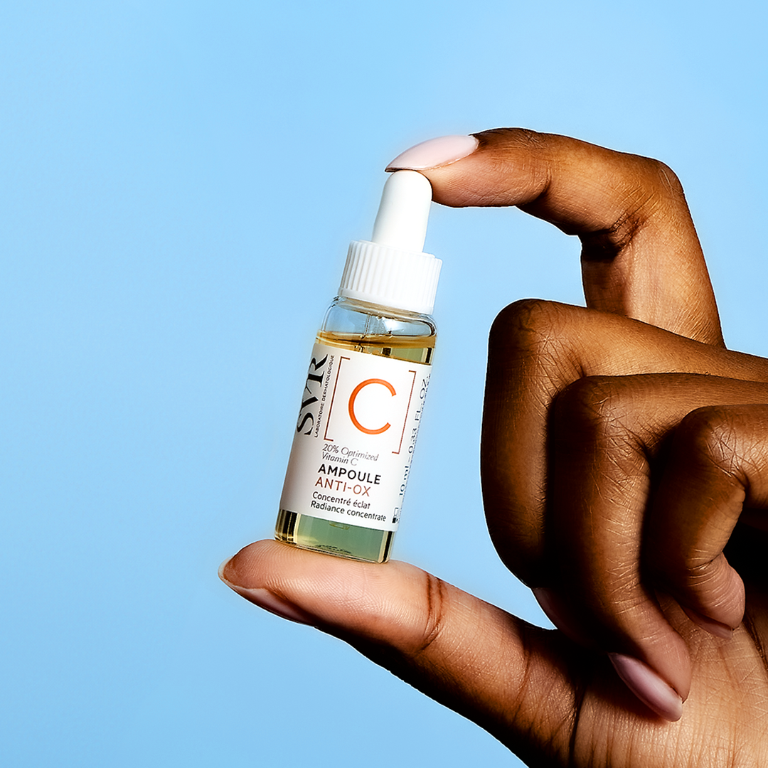SVR [C] Ampoule Anti-Ox, fingers holding the clear glass bottle against a blue background