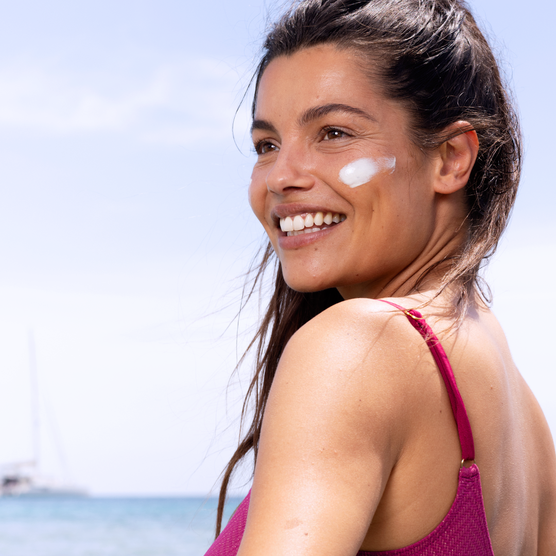 SVR Sun Secure, smiling woman by the sea with a streak of cream on her cheek