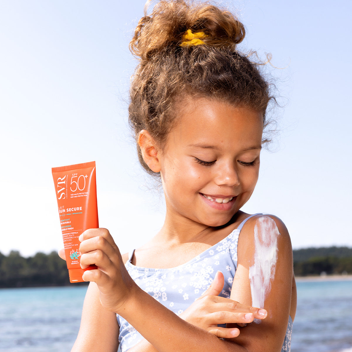 SVR Sun Secure, smiling girl by the sea spreading milk on her arm