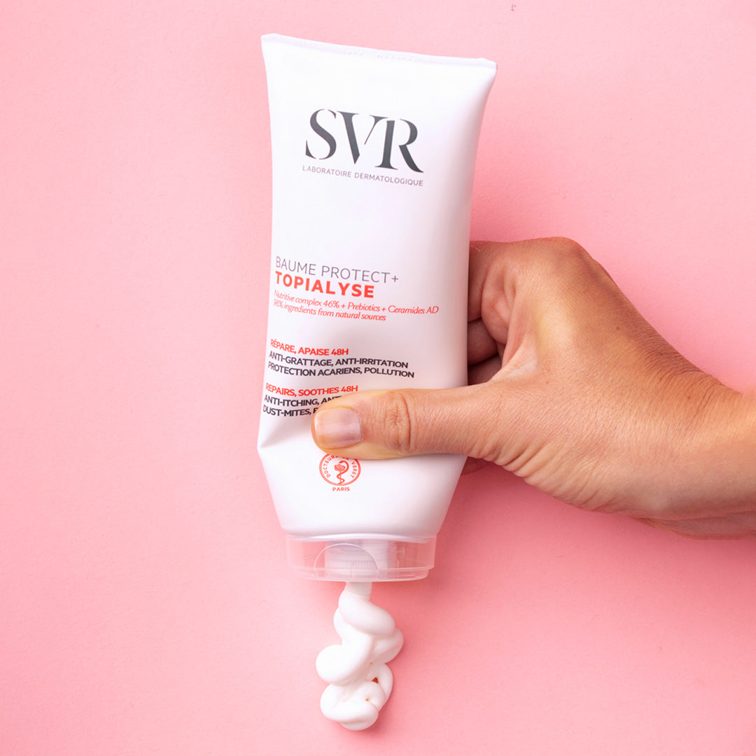 SVR Topialyse, hand squeezing balm from the tube on a pink background