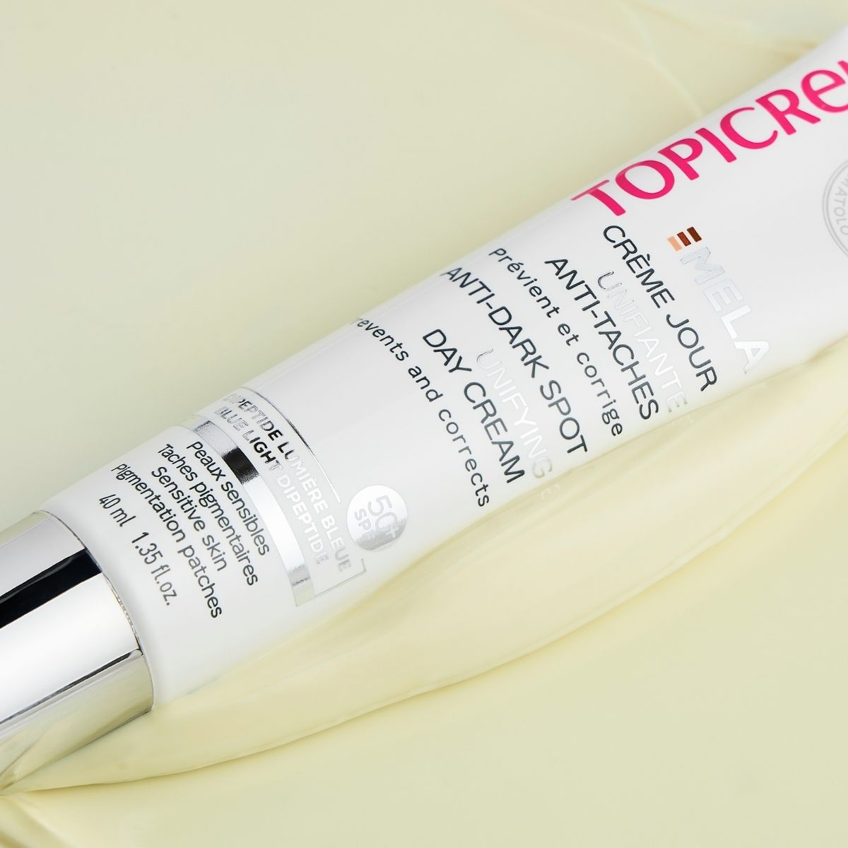 Topicrem MELA, tube lying on a bed of cream